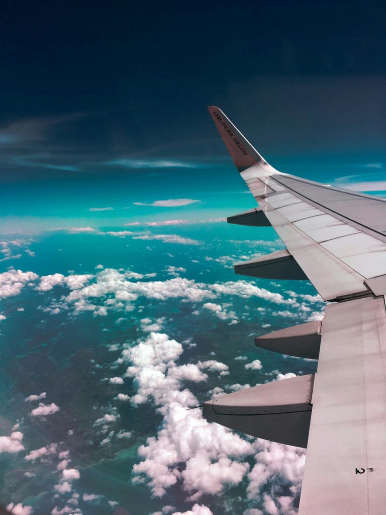 Aerial view of airplane wing over fluffy clouds with a deep turquoise sky.